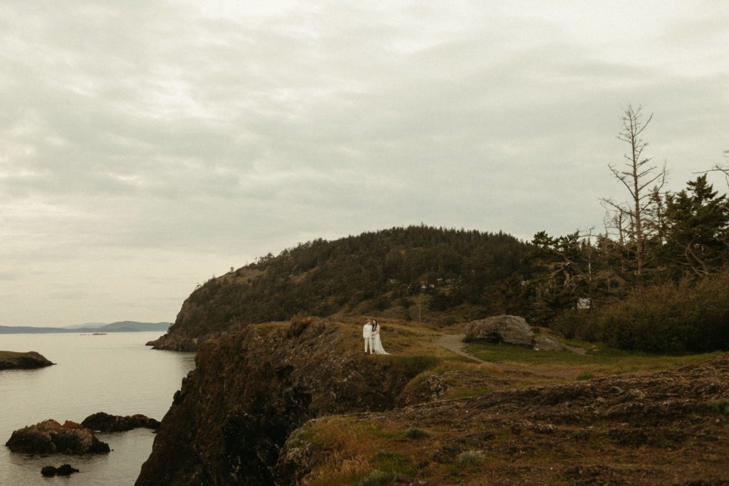 A couple standing side by side on a cliff at Deception Pass which is one of the best PNW engagement photo locations.