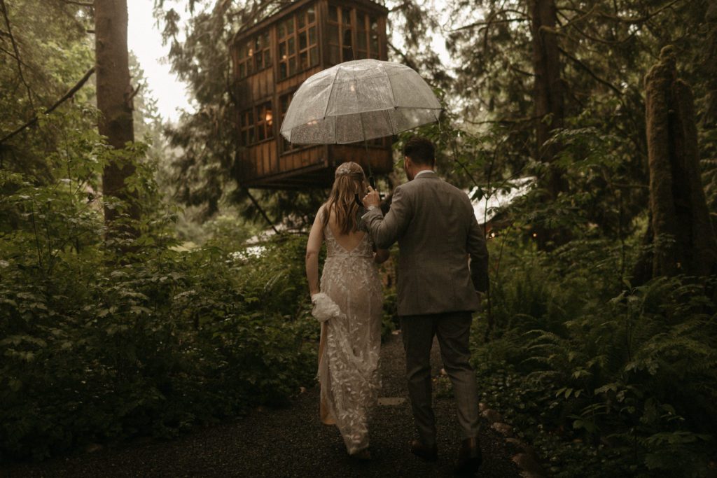 A couple waling on a path, holding a clear umbrella at the Treehouse Point wedding venue.